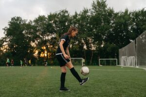 A young female soccer player kicking a ball on a field during sunset practice session.