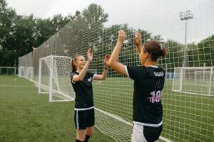 Two women football players high-fiving on a field, celebrating teamwork and success.