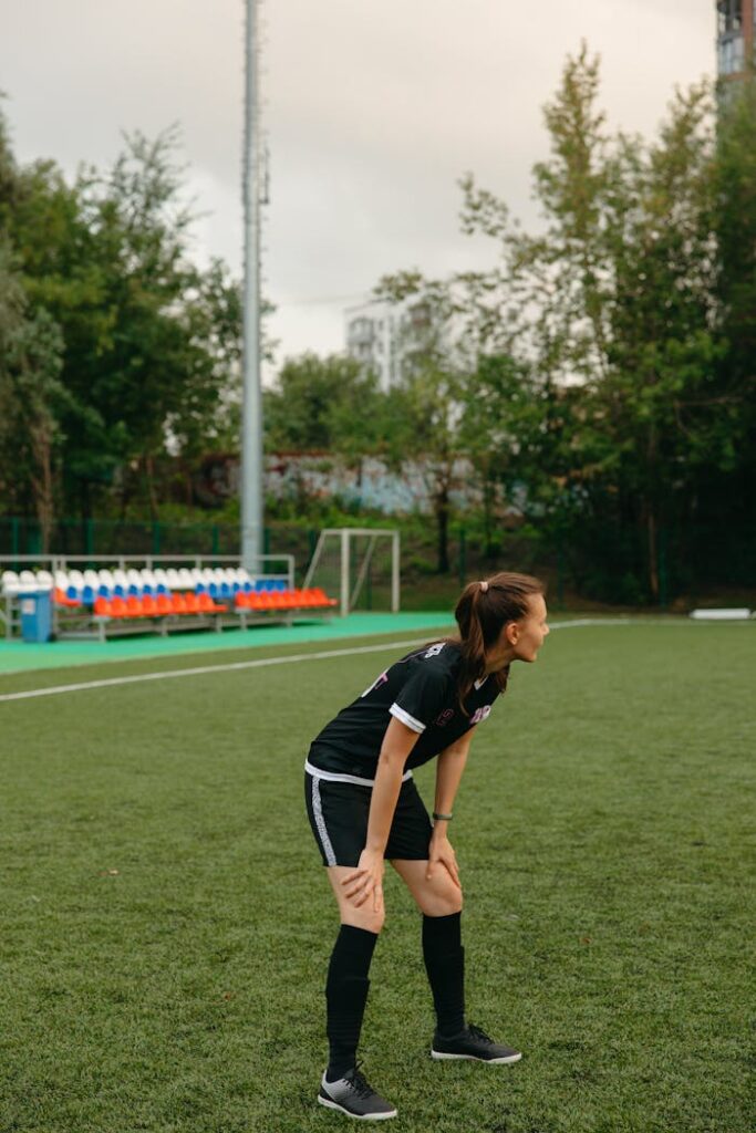 Young female soccer player taking a break during practice on a lush green field.